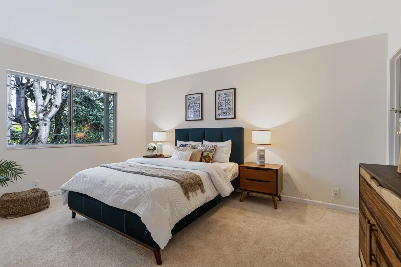 Bedroom with a blue upholstered bed and a wide window overlooking trees