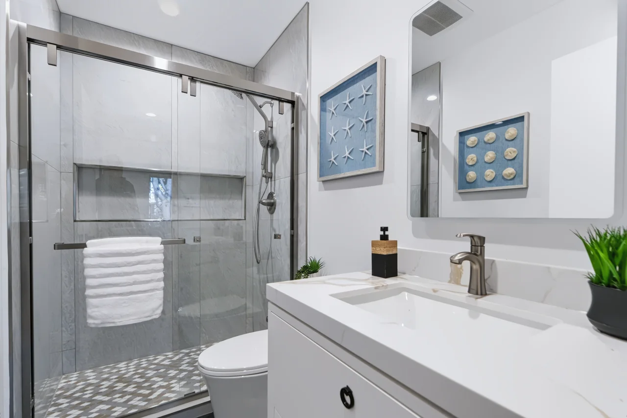 Bathroom with a glass shower, white vanity, and blue framed art