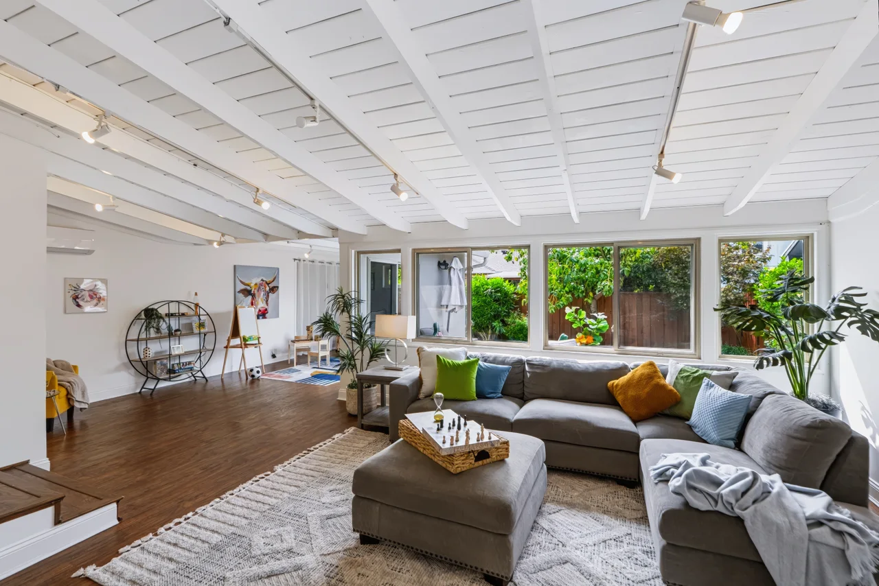 Sunlit living room with a white beamed ceiling, wood floors, and expansive garden windows