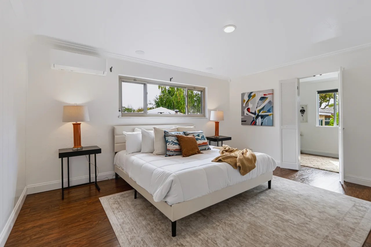 Bright bedroom with a white bed, wood nightstand, and garden-facing windows