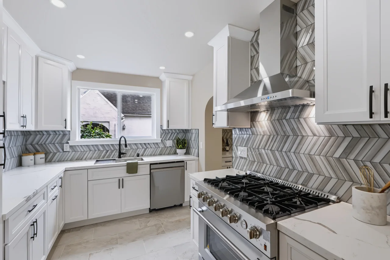 White kitchen with herringbone backsplash, stainless steel range, and a window above the sink