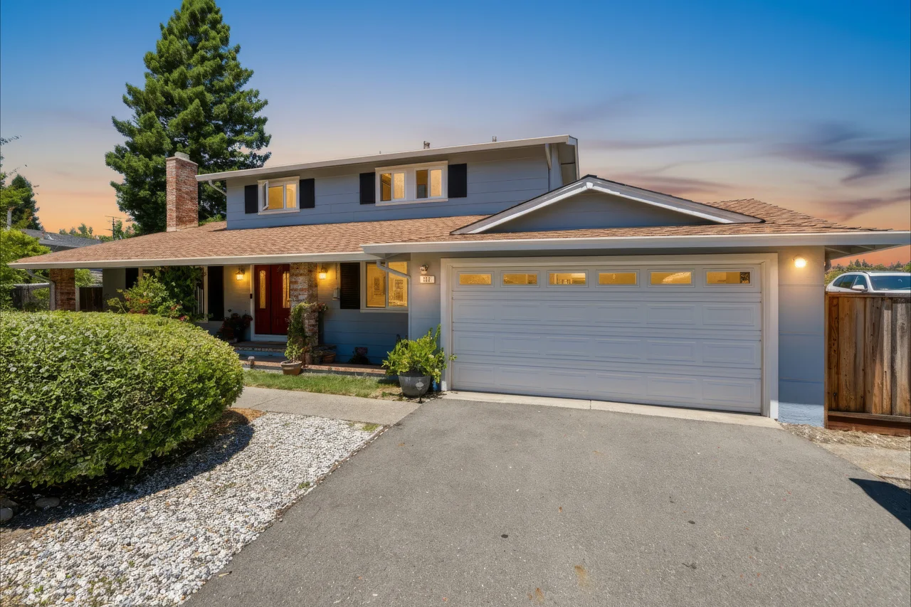 Two-story home with a wide driveway and warm exterior lights at sunset