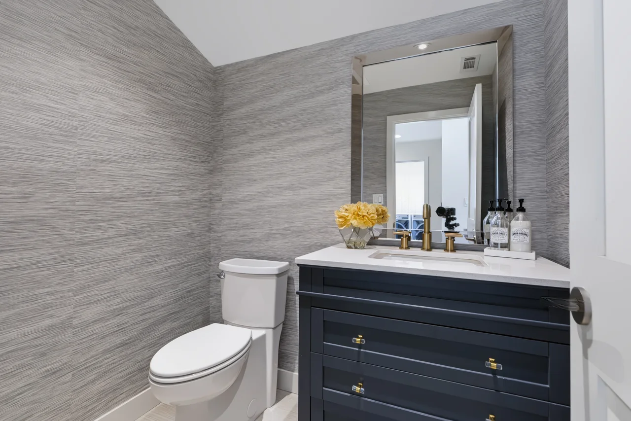 Powder room with a dark vanity, framed mirror, and textured wall covering