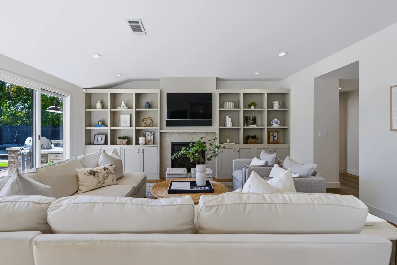 Bright living room with white sofas, built-in shelves, and large garden windows
