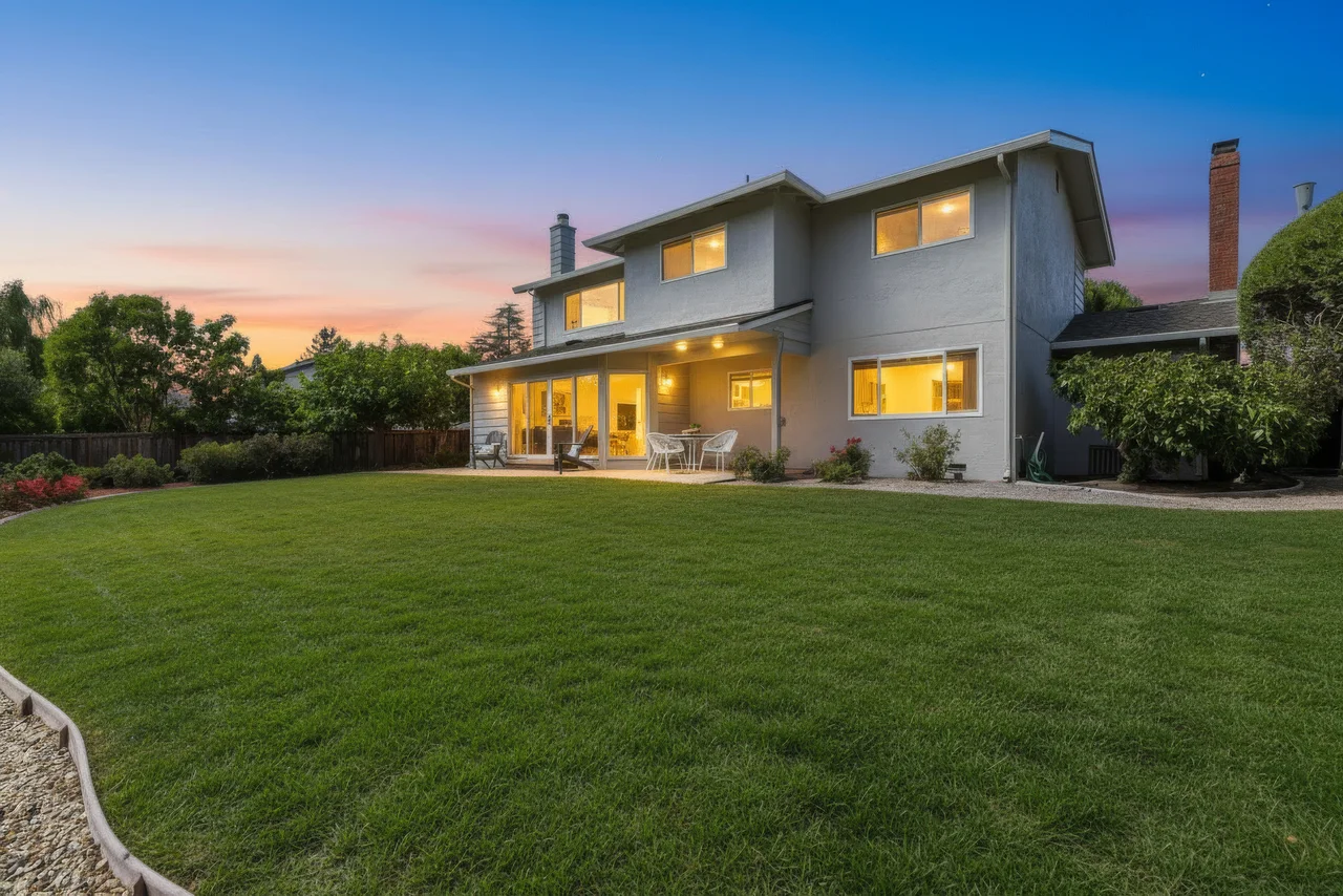 Two-story home with illuminated windows overlooking a green lawn at twilight